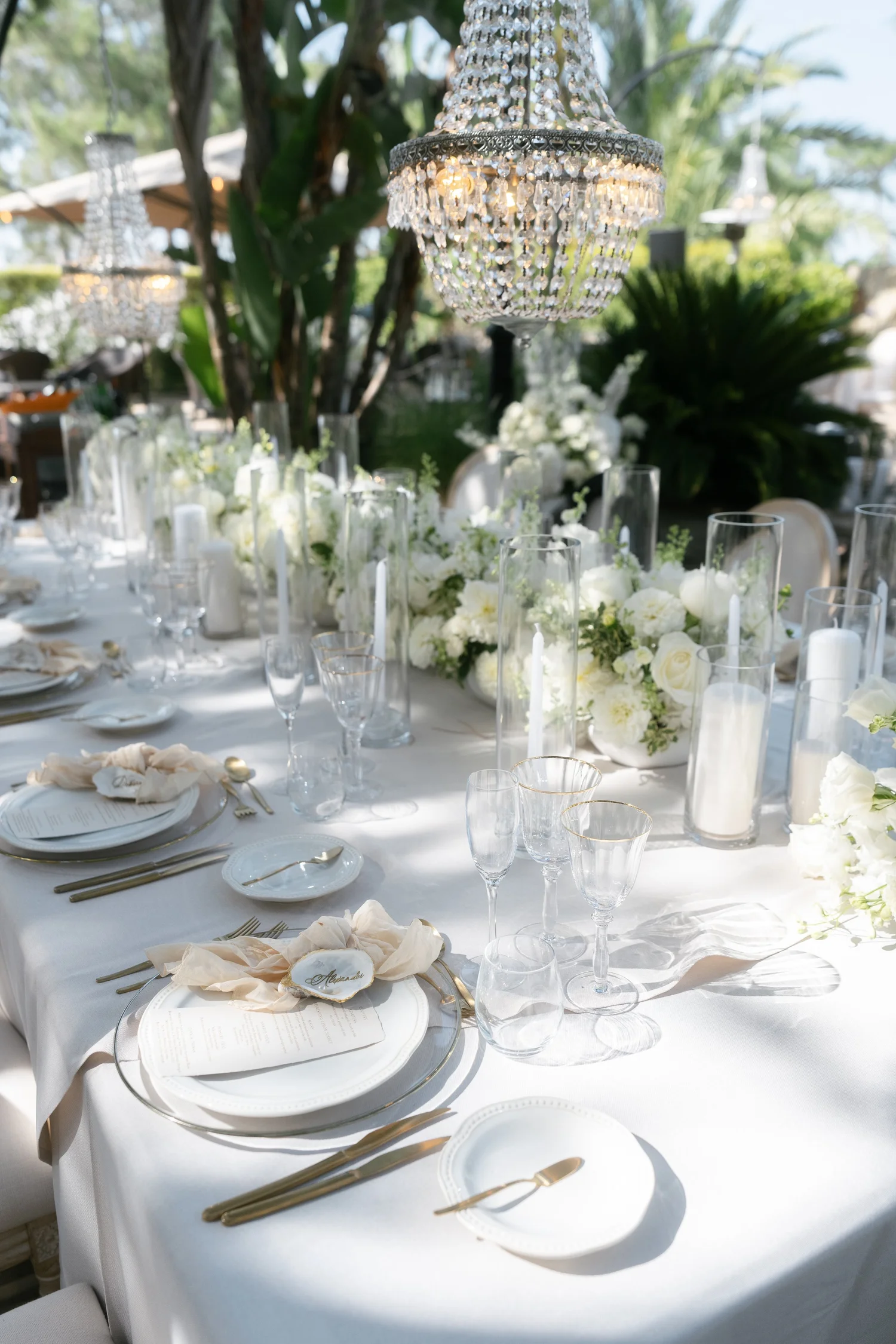 Luxury outdoor wedding table with white flowers, candles and crystal chandeliers