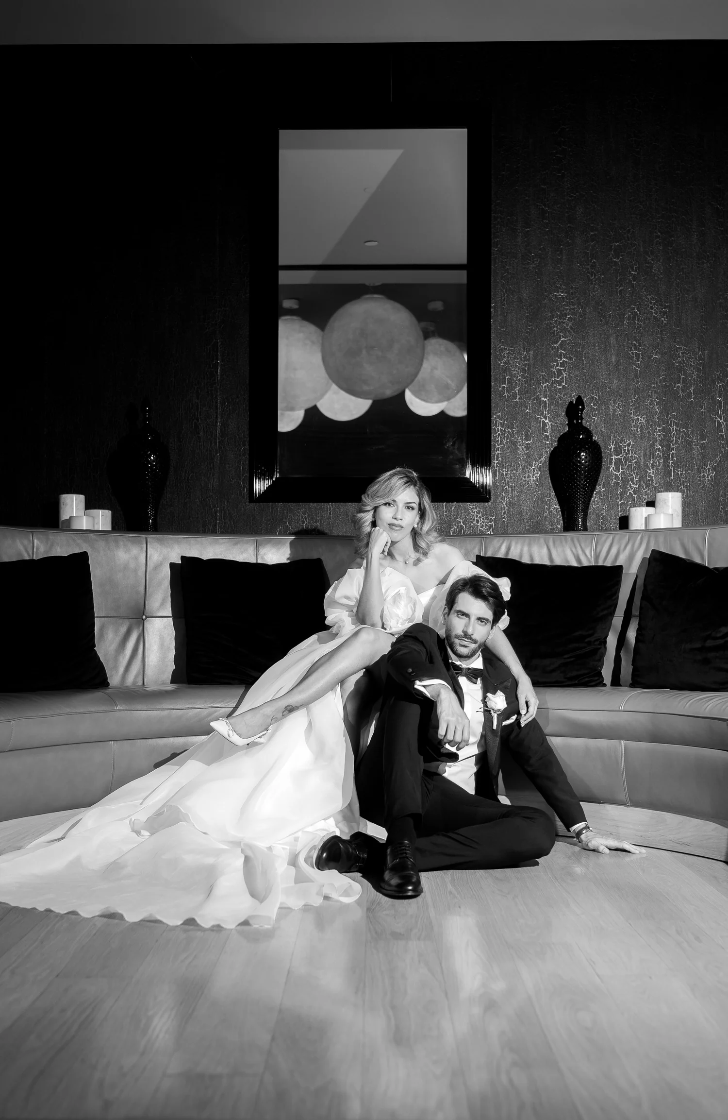 Black-and-white editorial portrait of a bride on a sofa and her groom seated on the floor beside her