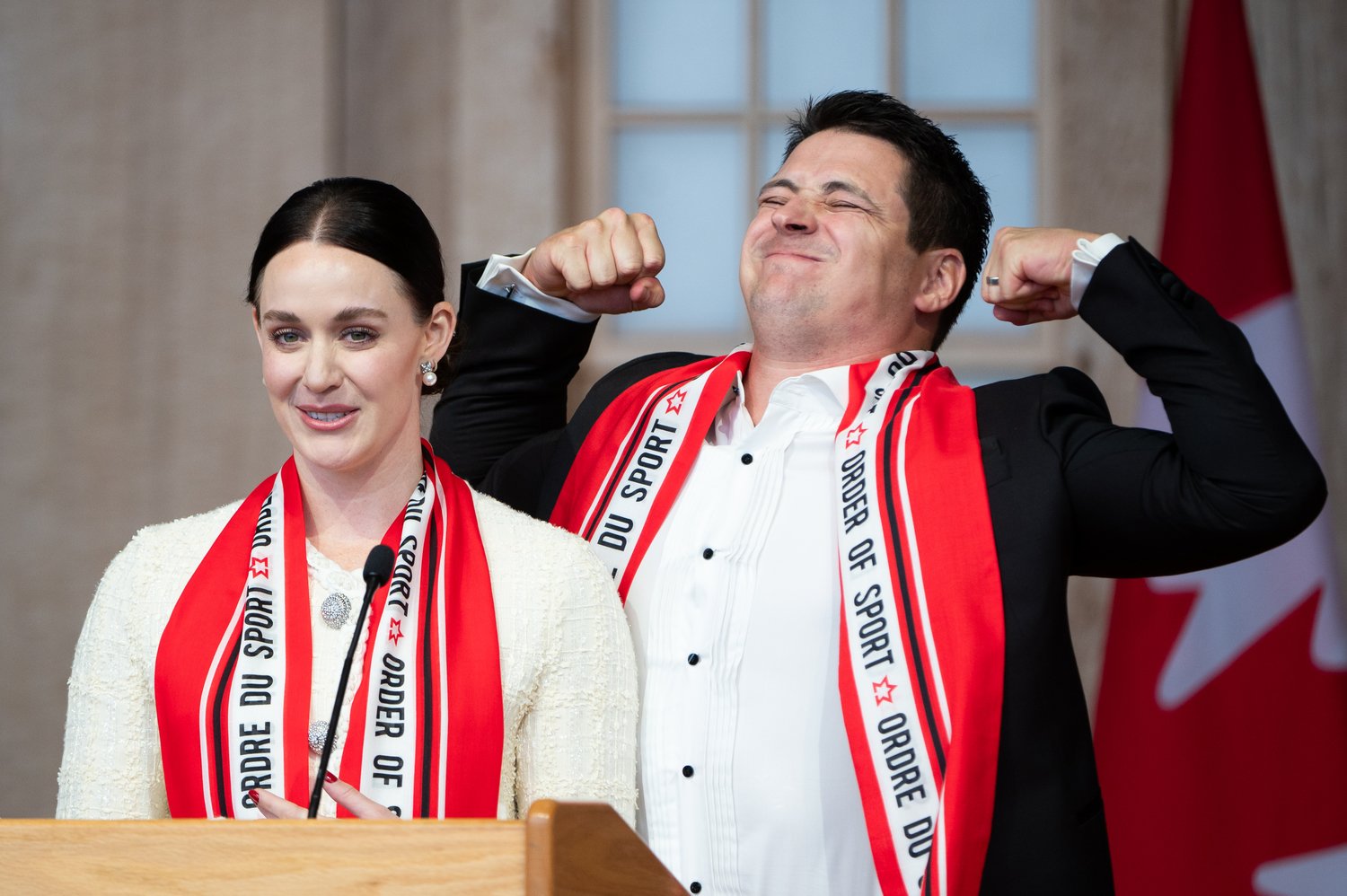  Canadian figure skater Scott Moir, right, flexes his muscles as he jokes on stage alongside partner Tessa Virtue, as they deliver remarks after receiving the Order of Sport during the Class of 2023 induction ceremony in Gatineau, Que., on Thursday, 