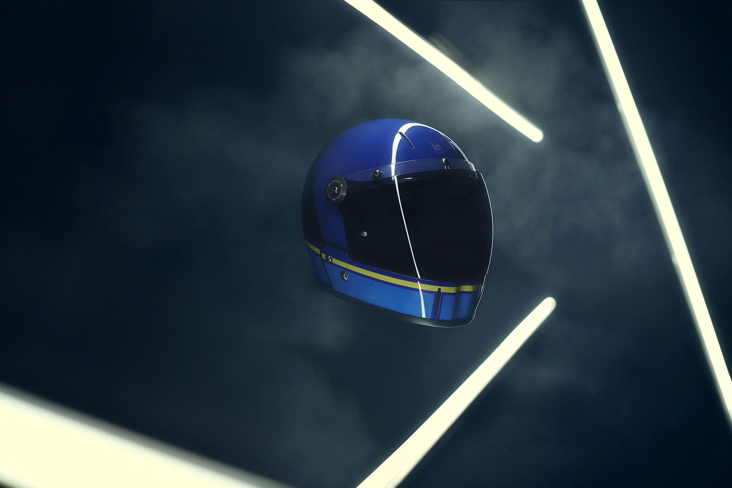 Blue racing helmet with a dark visor, illuminated by neon lights in a dark setting.