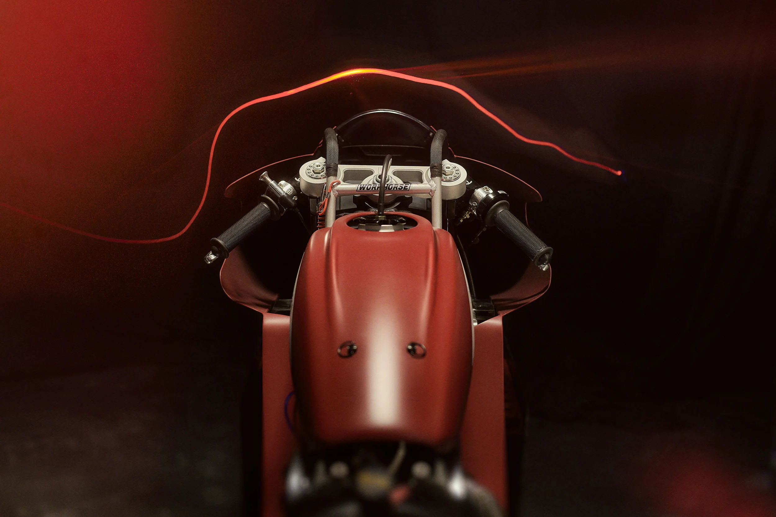 Top view of a red racing motorcycle cockpit with black handlebars against a dark background.