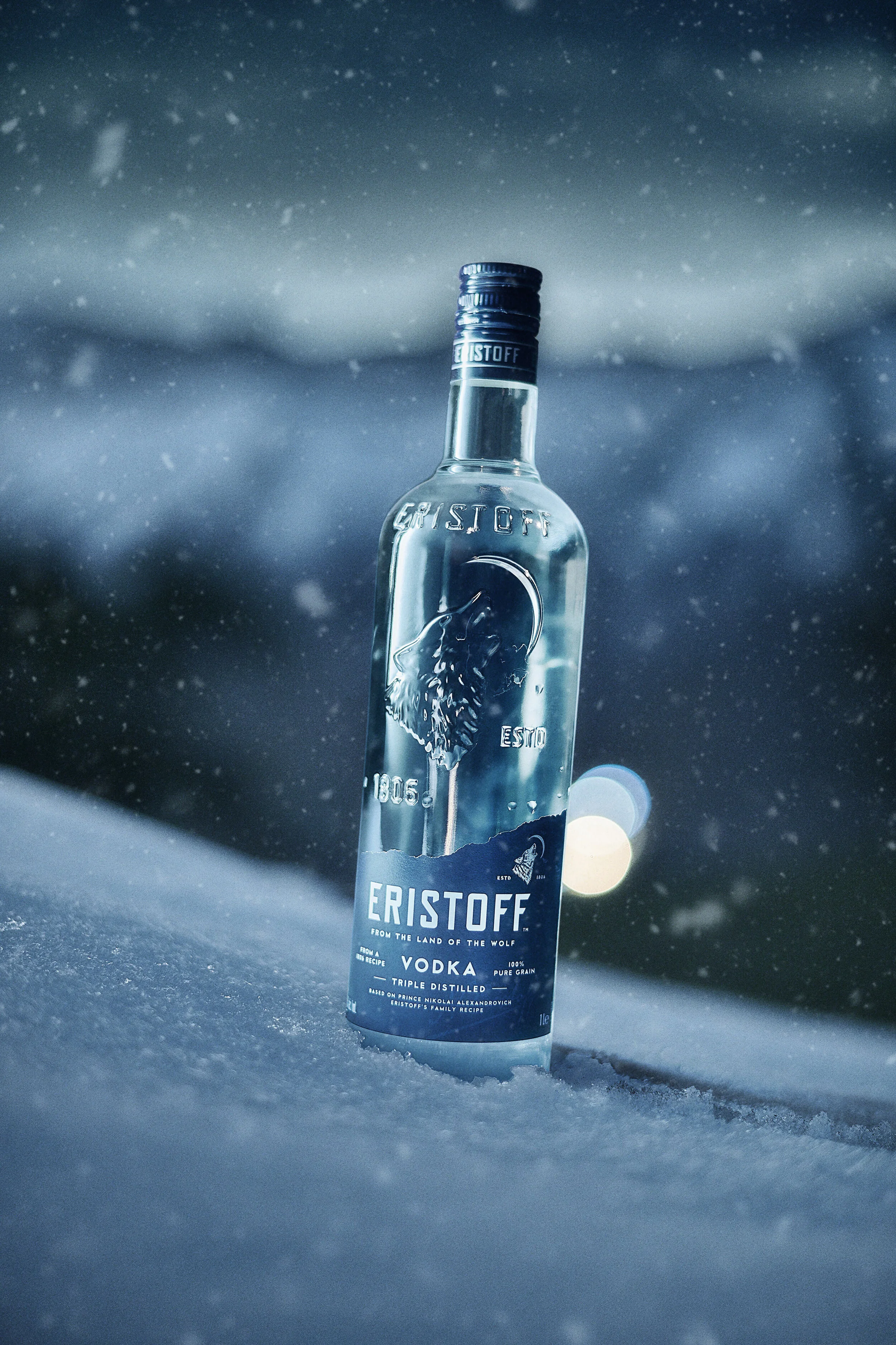 A clear glass bottle of Eristoff vodka standing upright on snow, with a blurred winter landscape in the background.
