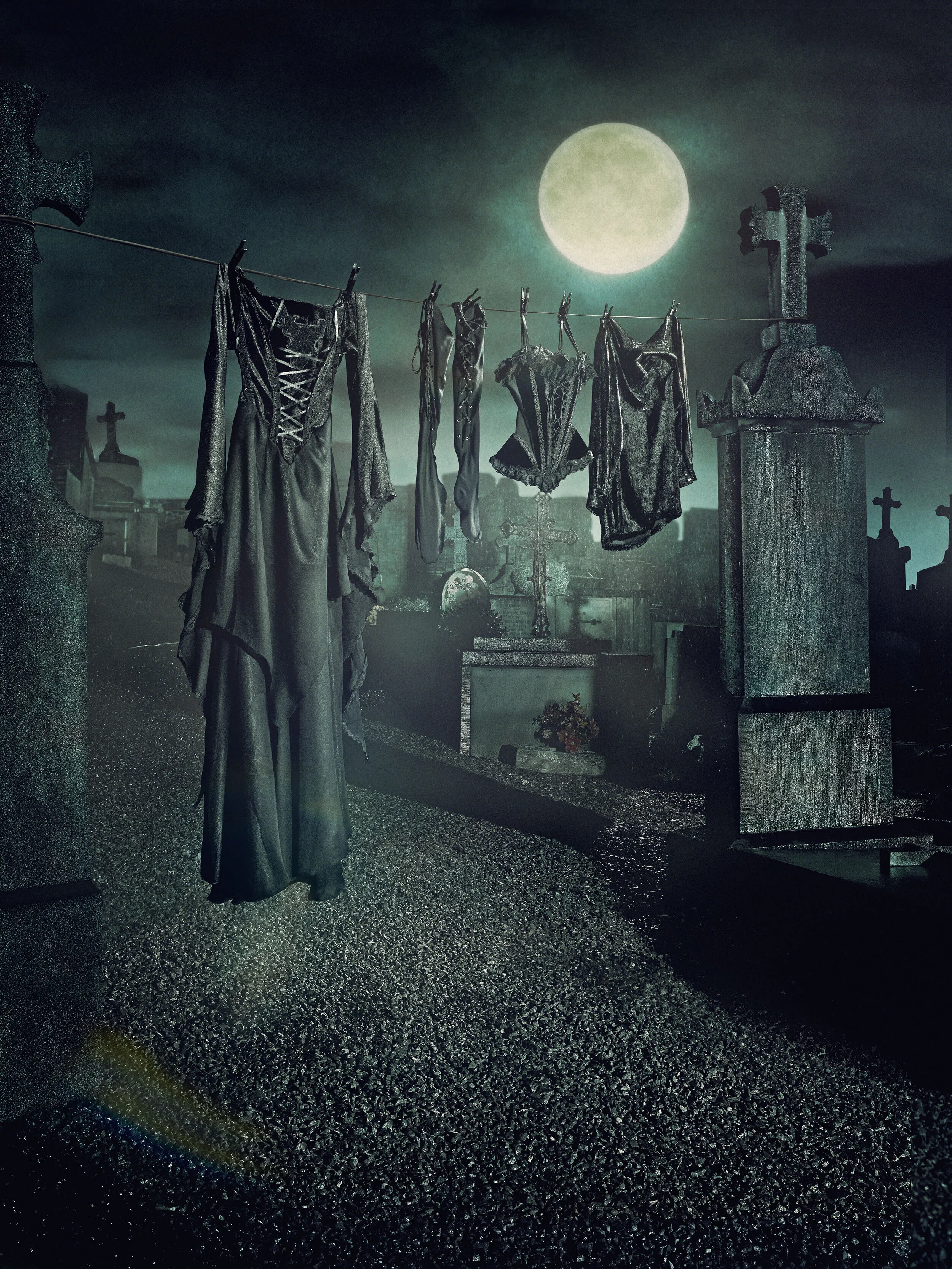 Clothes hanging on a line in a cemetery under a full moon with tombstones and crosses in the background.