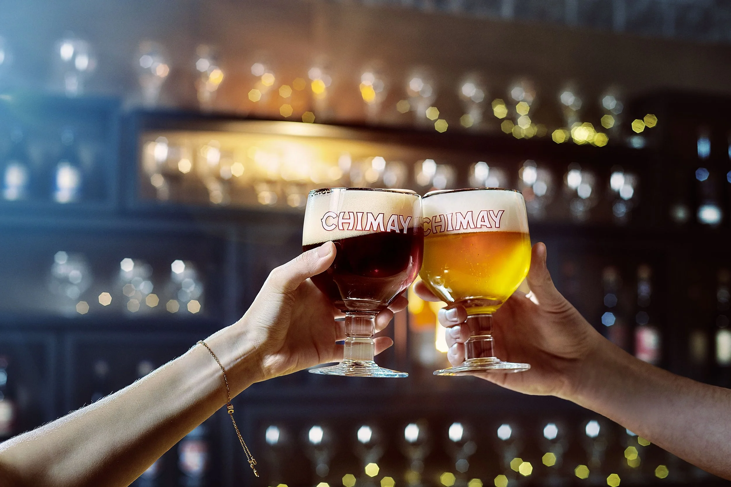 Two people clinking glasses of beer and wine in a bar or pub setting with blurred background lights.