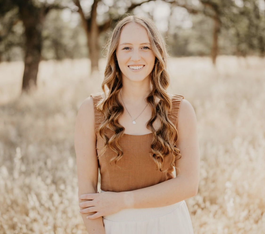 Ellie Gallaty stands in a field with a smile on her face and curls in her hair.