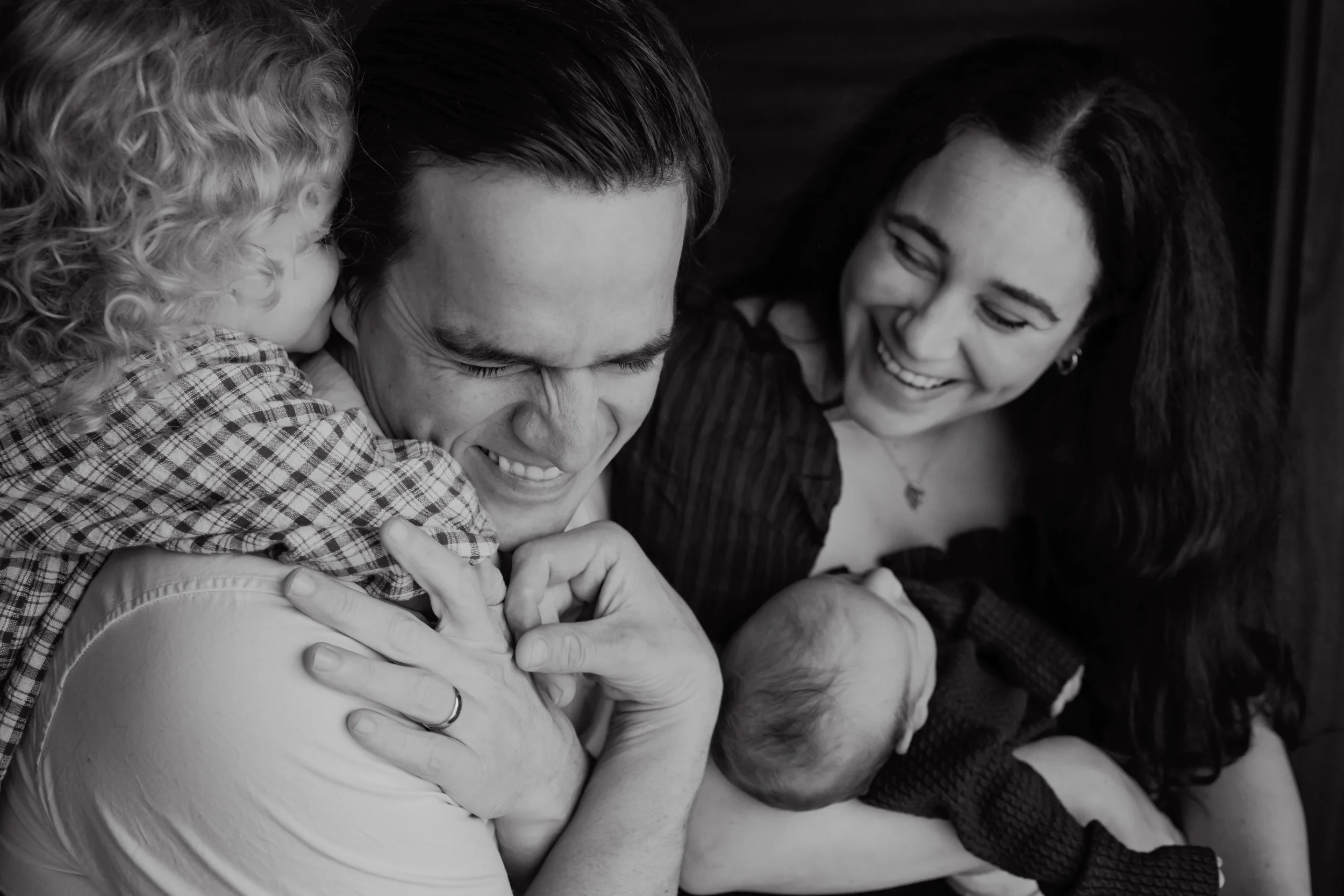 Two parents snuggled in close with their toddler and newborn