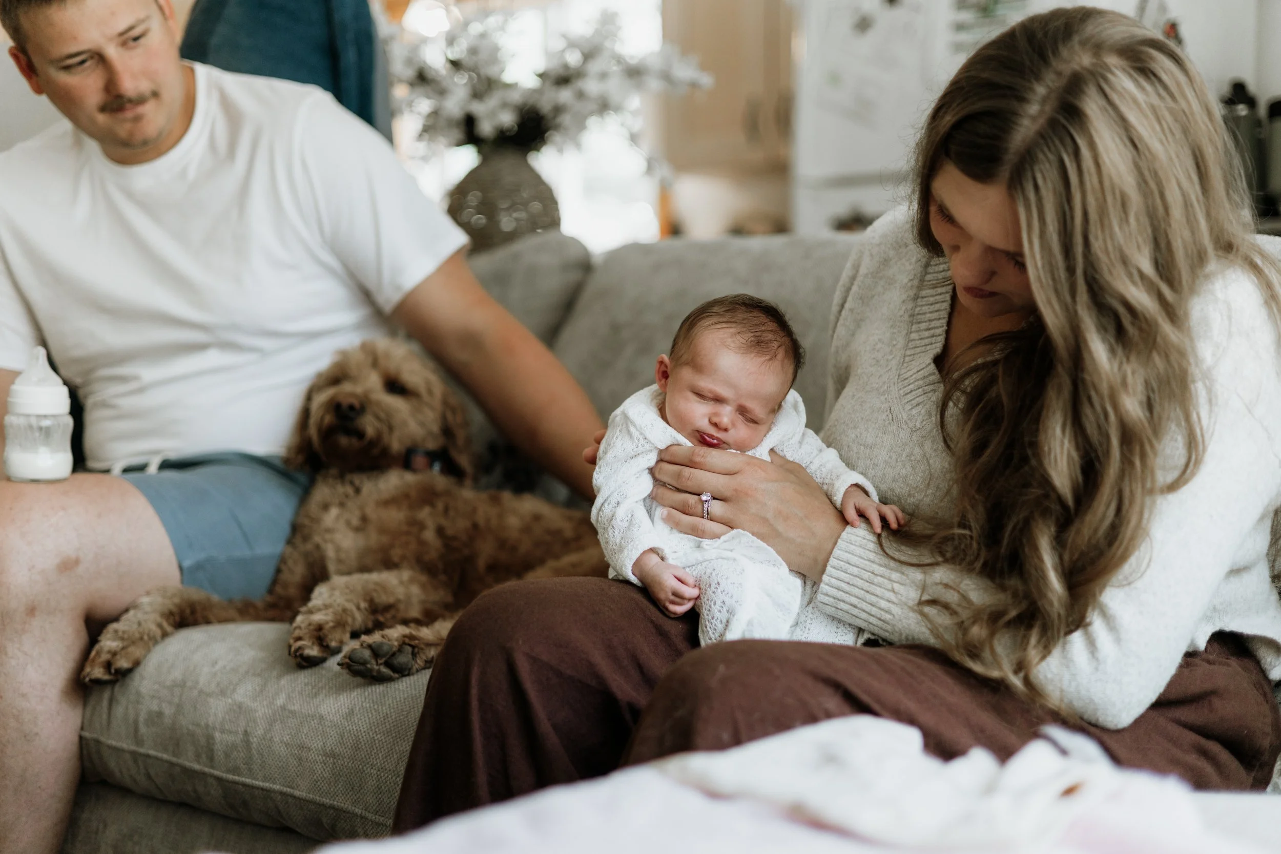 Mother holding a sleeping baby while her husband and dog snuggle nearby
