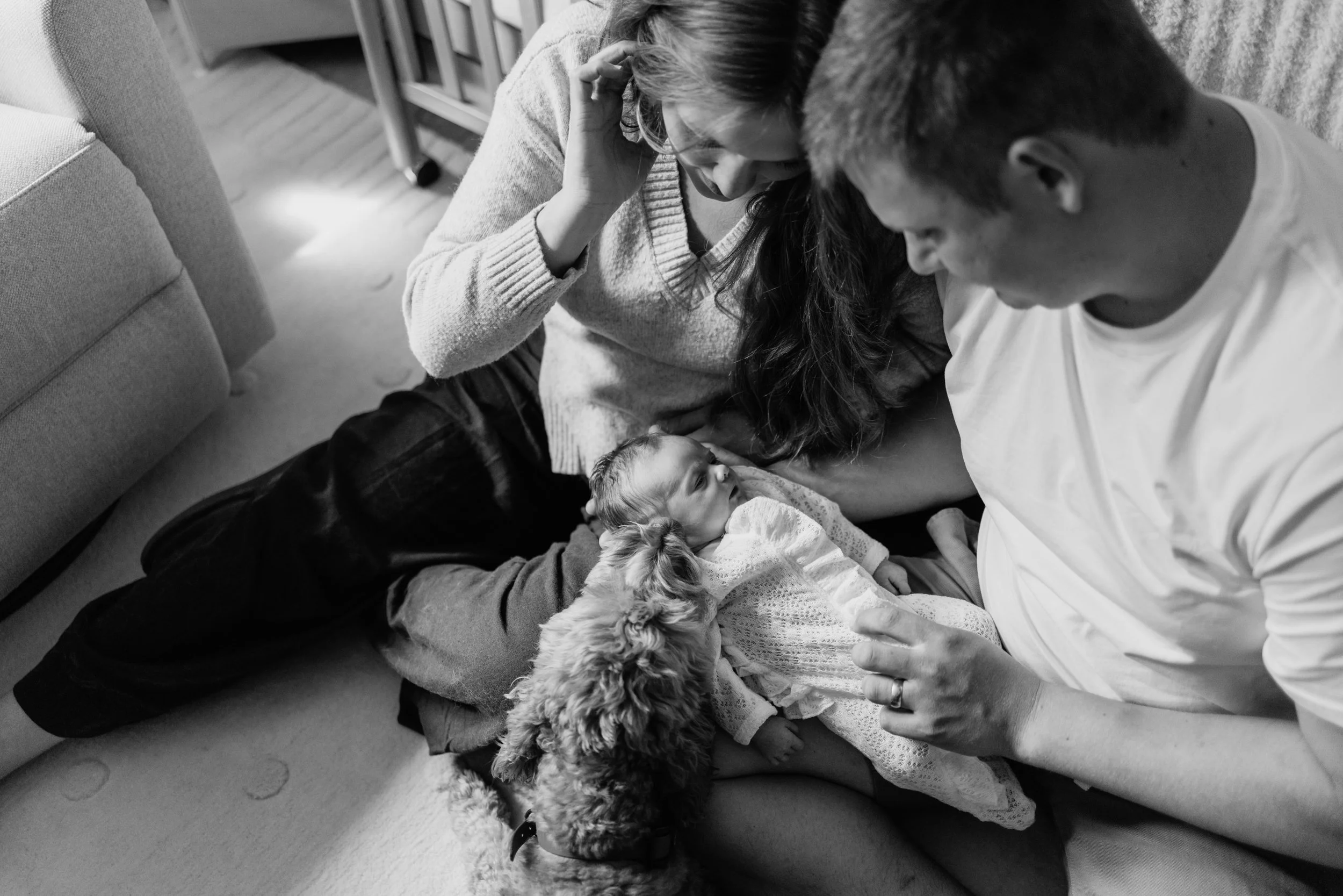 Sleeping newborn baby while parents and family dog snuggle in close.