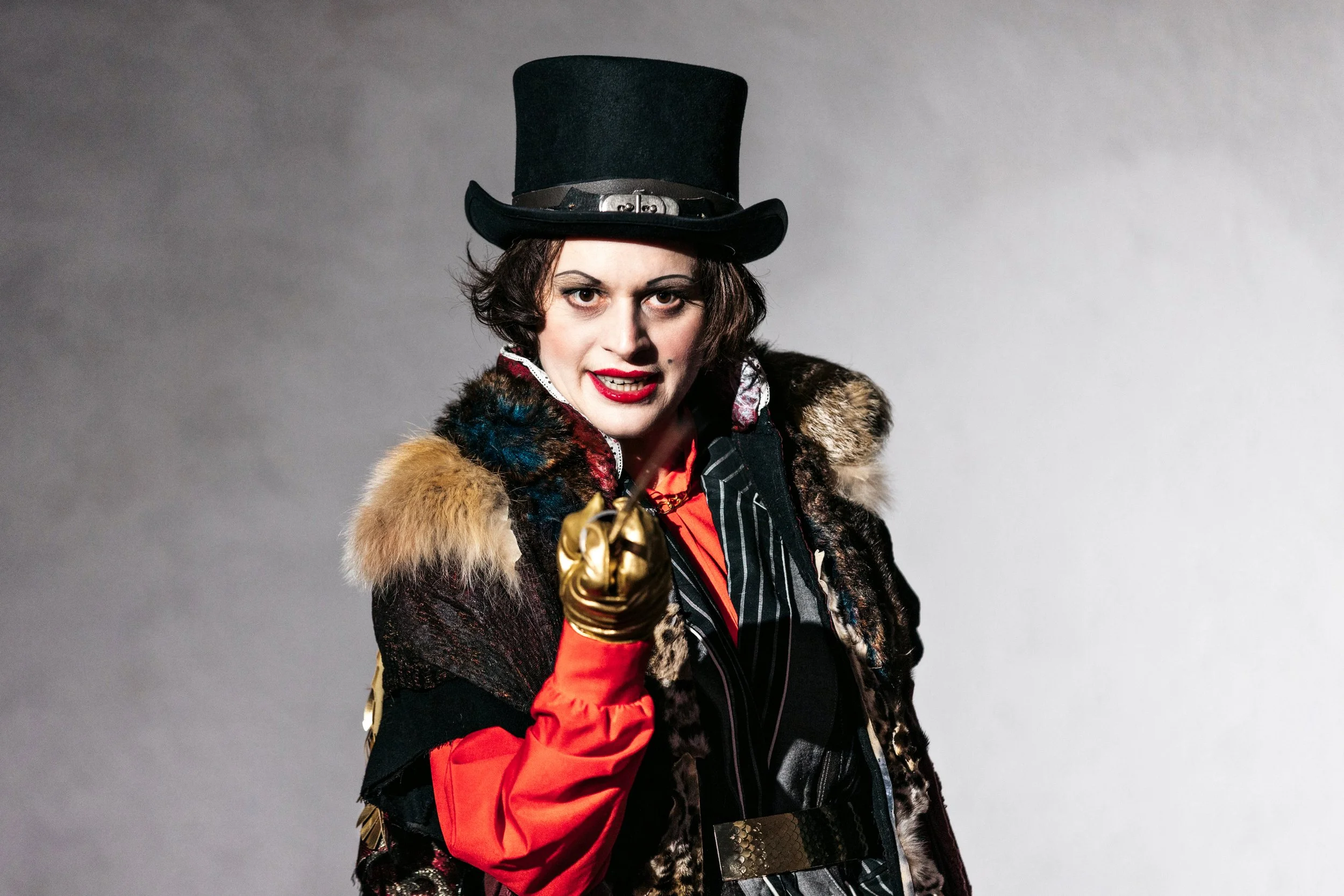 Actor in a costume wearing a black hat looking directly at the viewer.
