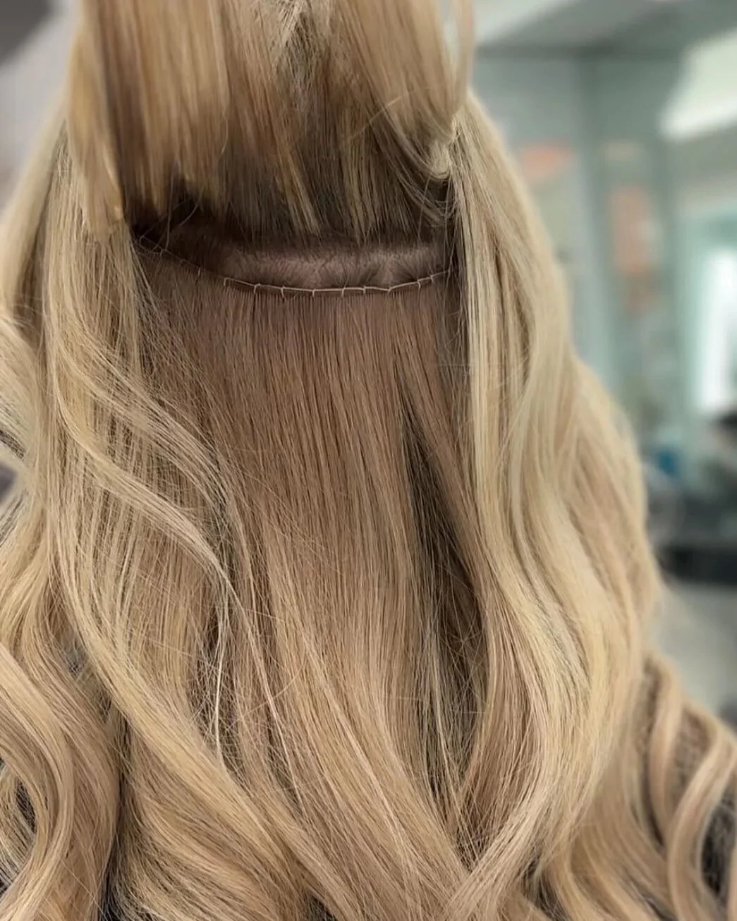 K-tip extensions strand-by-strand placement at Bellibone Salon Maywood NJClose-up of a section of blonde curly hair with a lace wig cap underneath.