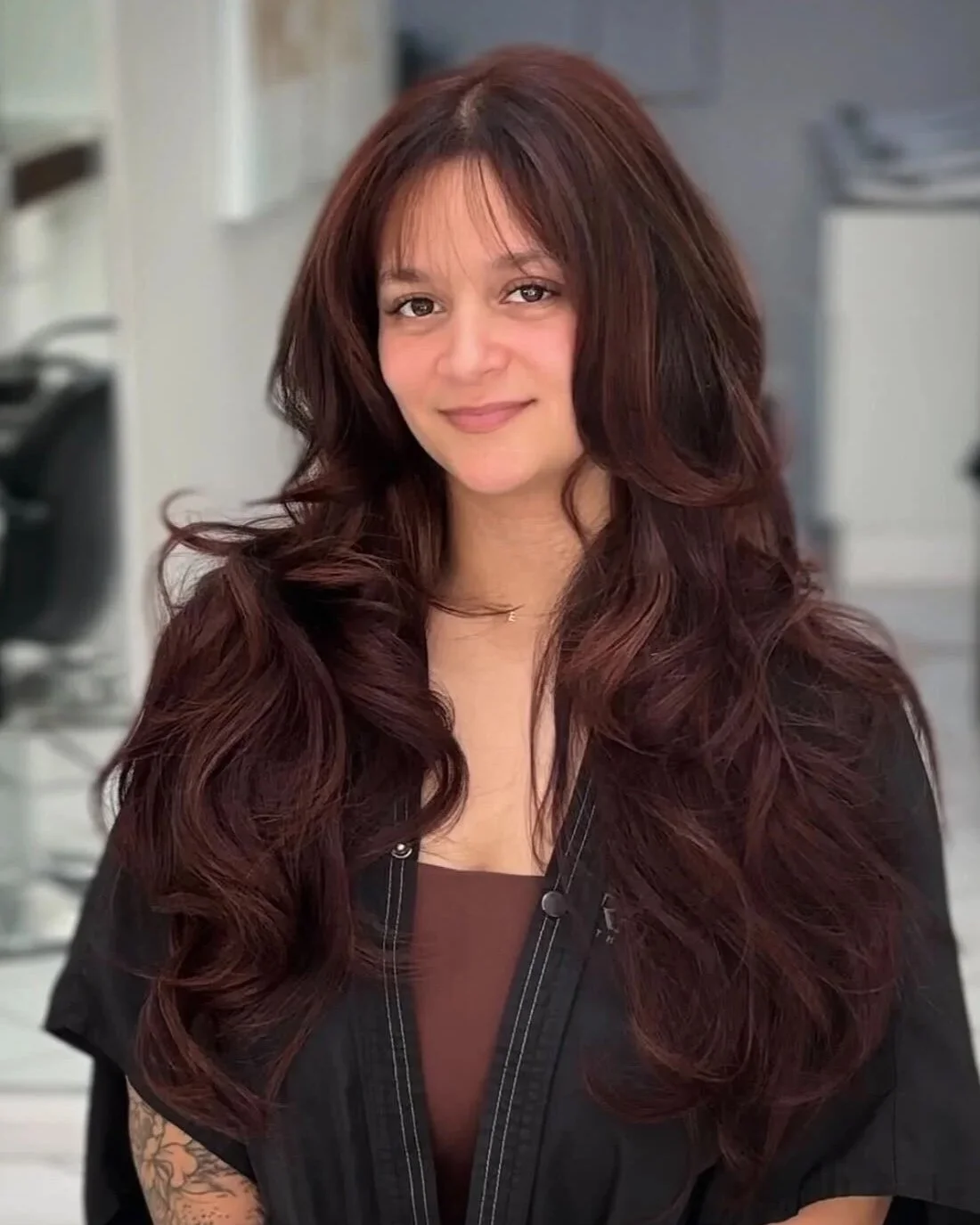 Hair extension transformation at Bellibone Salon in Maywood NJ A woman with long, wavy brown hair and a mild smile, sitting in a salon or clinic environment.