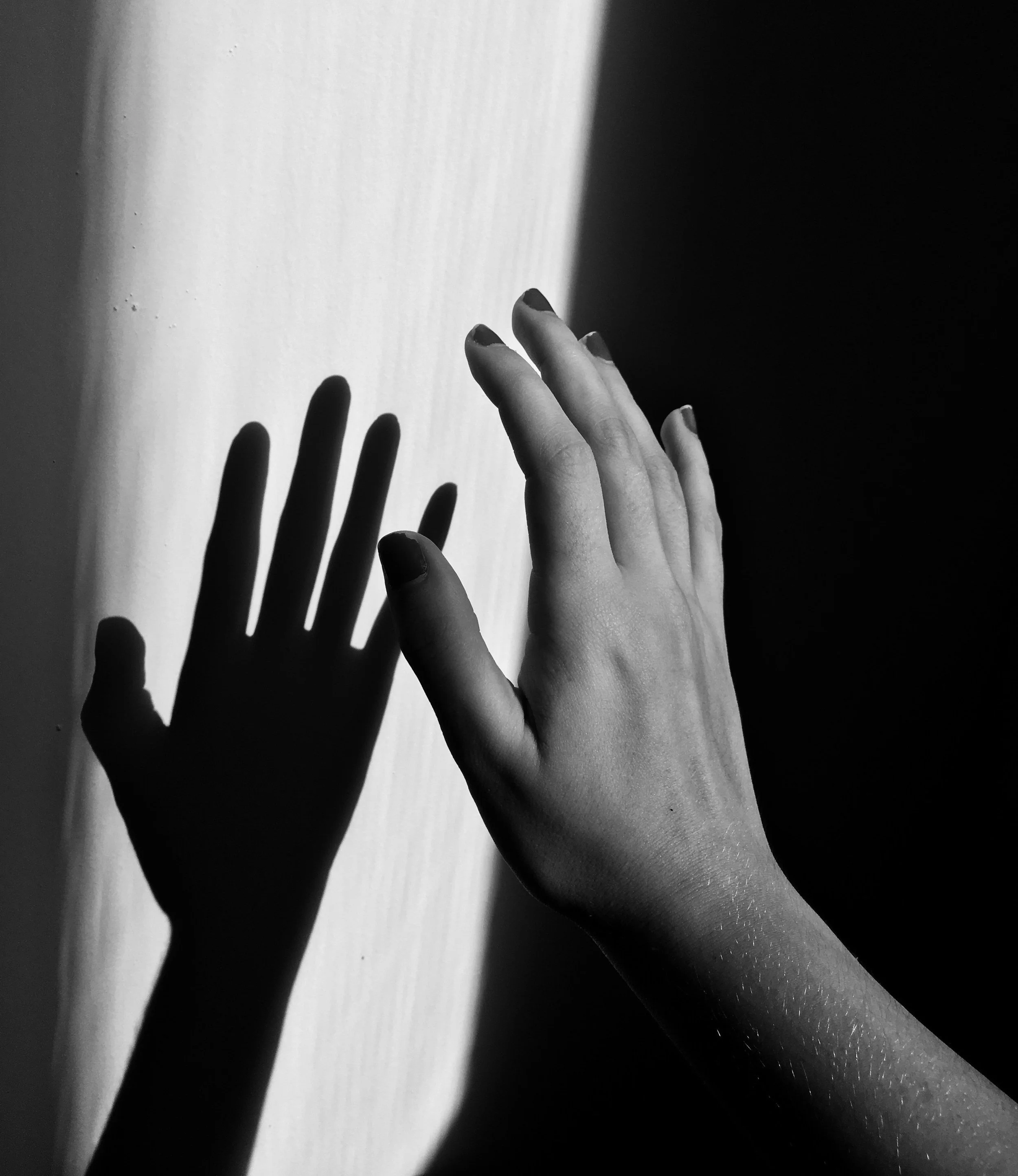 artistic black and white photo of woman's hand reaching for her shadow on the wall, on Kadhi Bo's article on Shadow Work