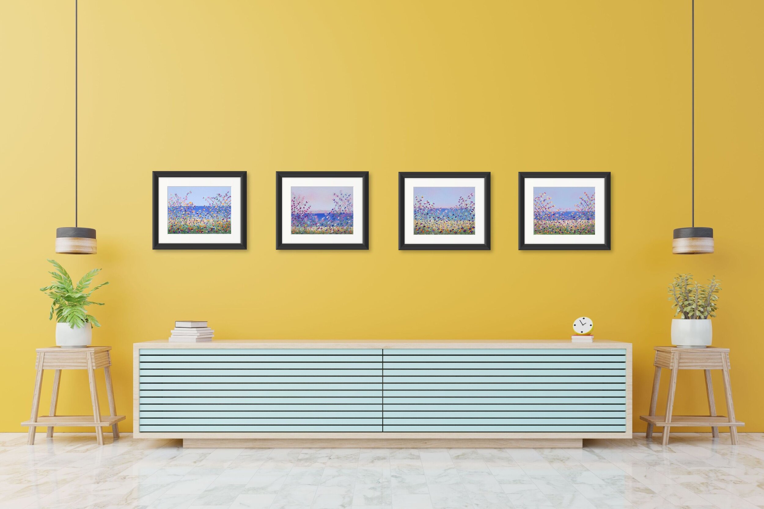 four floral paintings in black frames on yellow wall above low light wood table with teal stripes