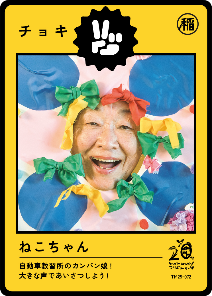 A woman smiling with her face surrounded by colorful bows and paper decorations, on a bright yellow card with Japanese text.