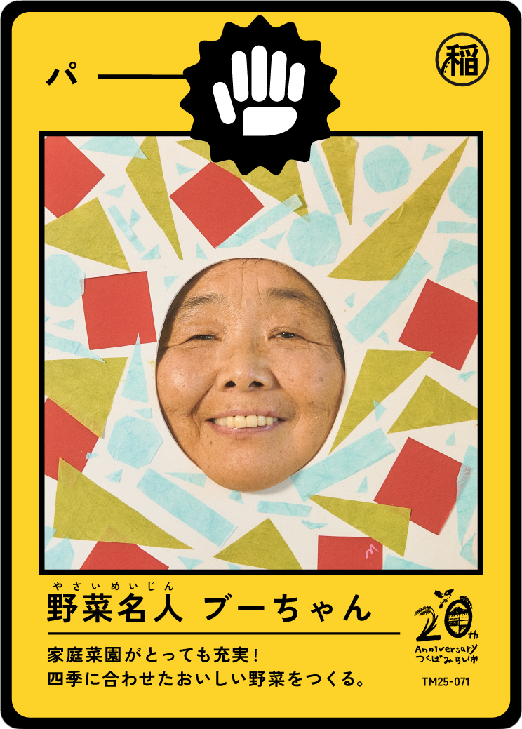 A person with a smiling face looking through a colorful paper frame with geometric shapes. The frame looks like packaging for a product, with Japanese text and symbols, including a large black icon of a hand in a fist and a logo celebrating a 20th an