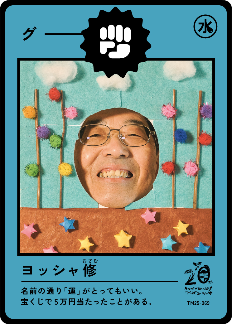 A decorative photo booth frame with a man's face in the center, smiling broadly, wearing glasses. The background includes colorful pom-poms and star-shaped decorations. The frame resembles a Japanese trading card with text and logos, celebrating a 20