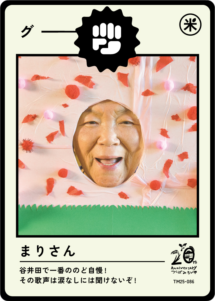 A woman with a smiling face peeking through a hole in a pink, flower-decorated paper costume, resembling a strawberry, with Japanese text and a 20th anniversary logo.