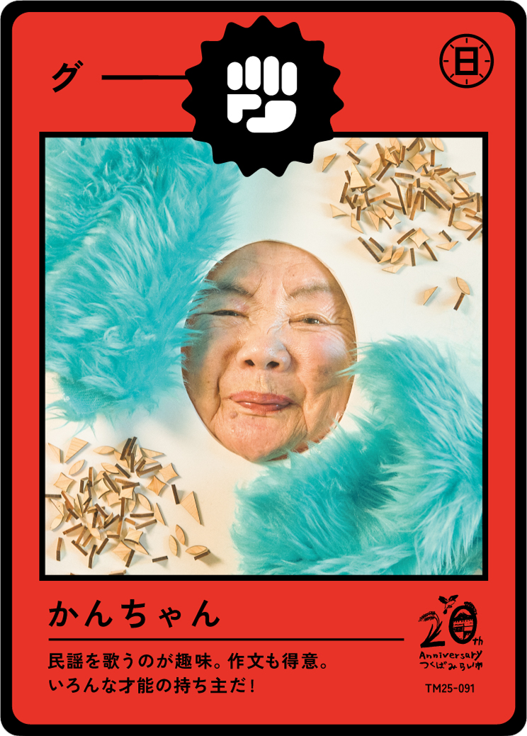 A playful card with a person sticking their tongue out through a cutout hole, surrounded by teal faux fur and scattered small wooden pieces, with Japanese text and celebratory symbols for an anniversary.