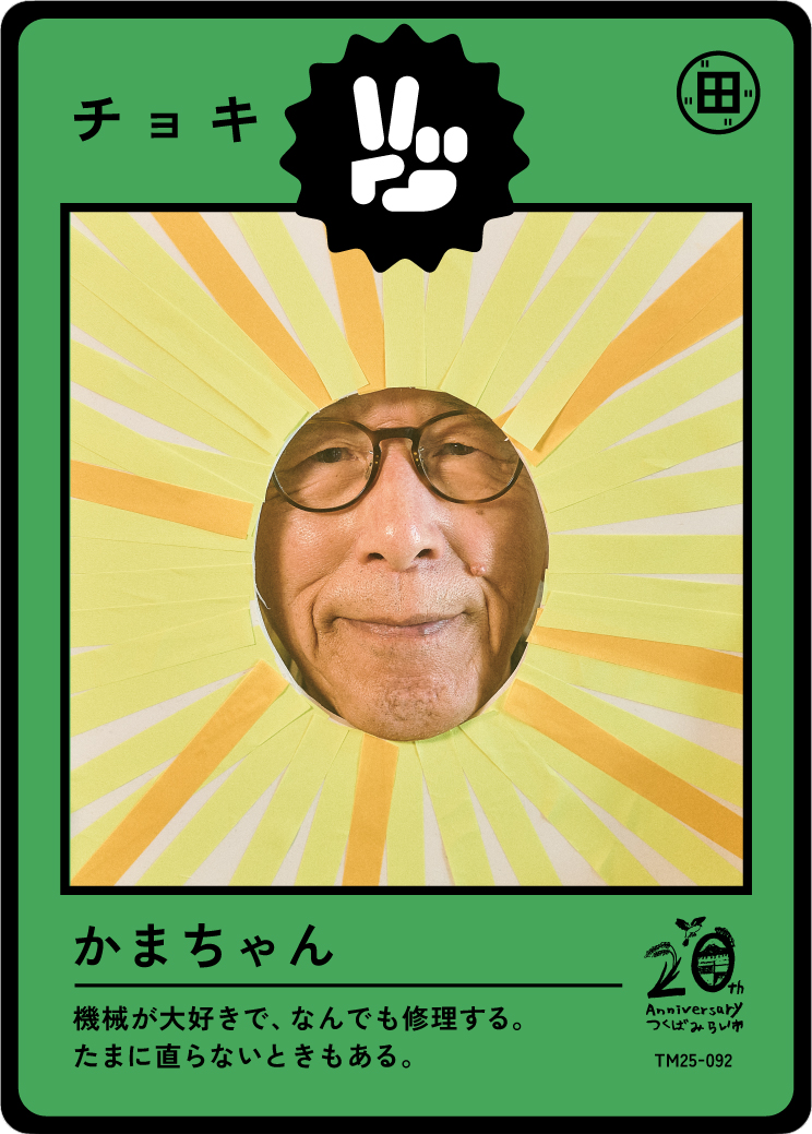 Photo of a man with glasses looking through a circular cutout with yellow and orange rays behind his face, resembling a sun or lightburst, on a green background with Japanese text and a logo.