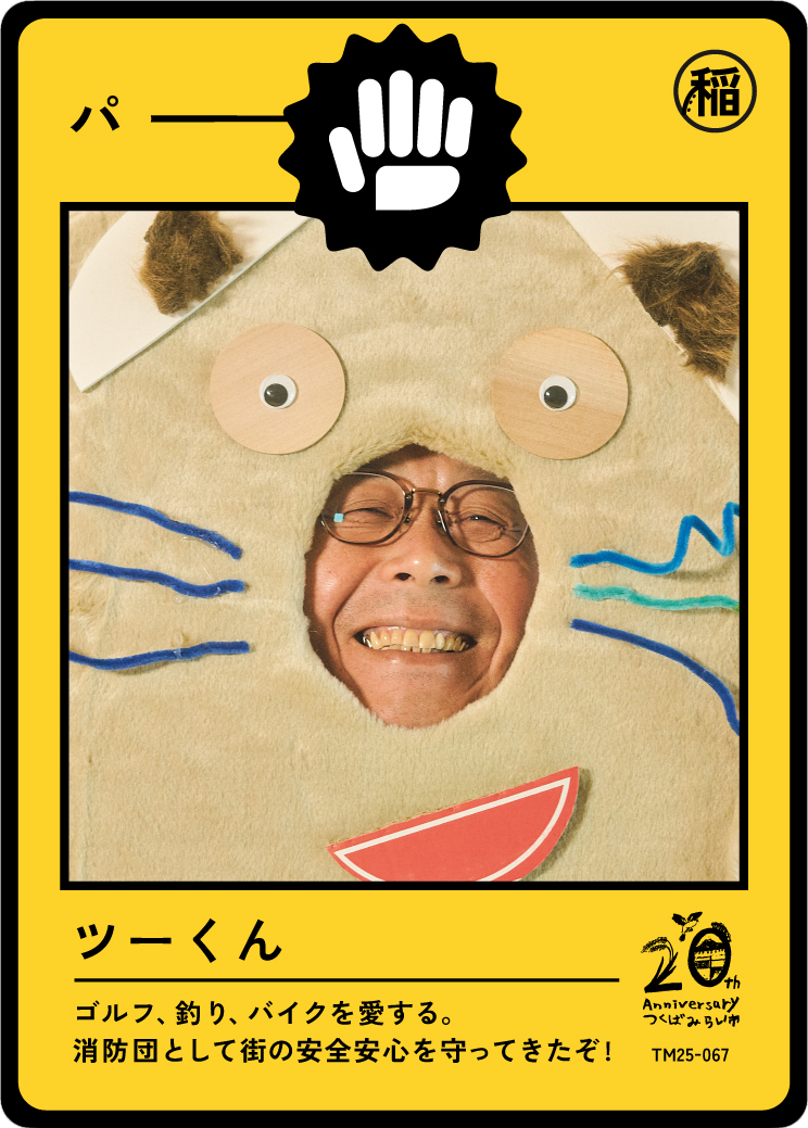 A person smiling through a cutout of a cartoon dog costume with blue lines and googly eyes. The costume has a yellow background with black Japanese characters and a logo celebrating a 20th anniversary.