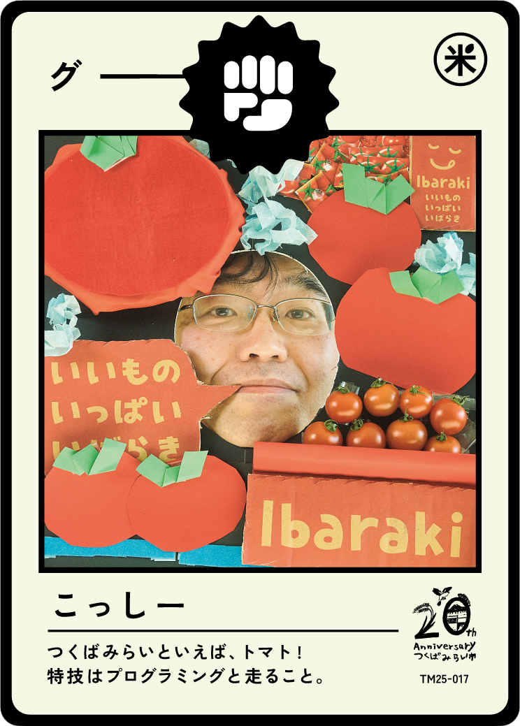 Photograph of a person looking through a collage of tomato-themed craft materials, including paper tomatoes, origami boxes, and real tomatoes, with Japanese text and a logo celebrating Tsubaki's 20th anniversary.