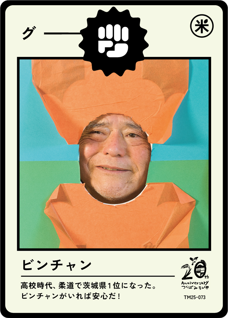 A person with a smiling face peeking through an orange paper cutout shaped like a food container with a lid. The background is a mix of blue and green colors. The image is styled like a trading card with some Japanese text and symbols.
