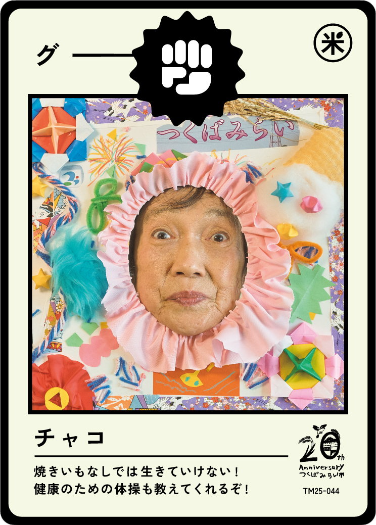A woman with a cheerful expression looking through a circular pink paper frame surrounded by colorful origami and craft decorations, with Japanese writing and a 20th-anniversary logo in the bottom right corner.