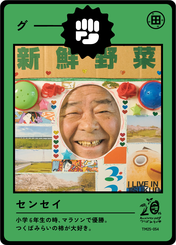 A person with a wide smile and slightly squinted eyes looking through a circular cutout in a collage frame decorated with small hearts, stars, and photographs of landscapes and cherry blossoms, signifying a celebration or tribute. The collage is moun