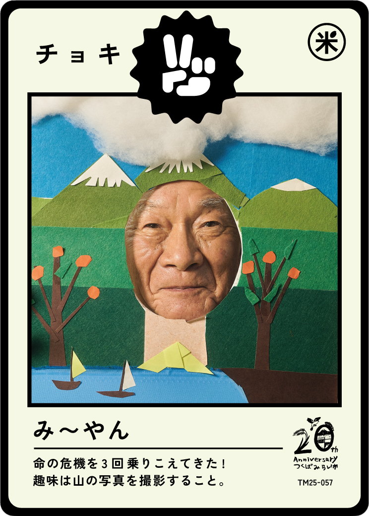 A paper craft image featuring a cutout of an older man's face, set against a scenic background of paper mountains, trees, water with sailboats, and clouds. The scene is topped with a black and white graphic and Japanese text, celebrating a 20th anniv