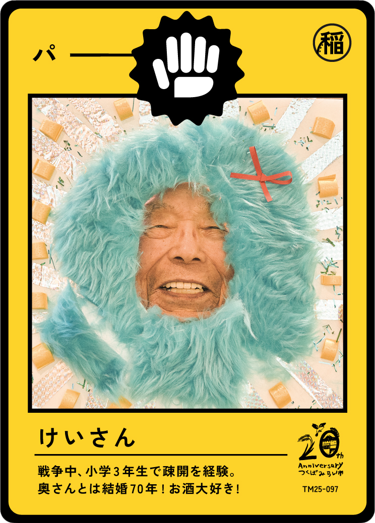 A humorous card featuring an elderly person with a smiling face, surrounded by a fluffy turquoise frame resembling a costume or mask, with Japanese characters and a black and white icon of a hand in the top center, and small decorations around the fa