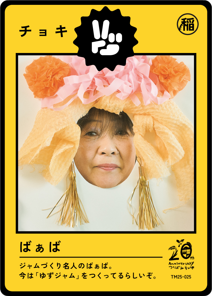 Person's face looking through a paper craft frame resembling a peach-colored traditional costume with tassels, paper flowers, and ribbons, framed by a yellow background with Japanese text and branding.