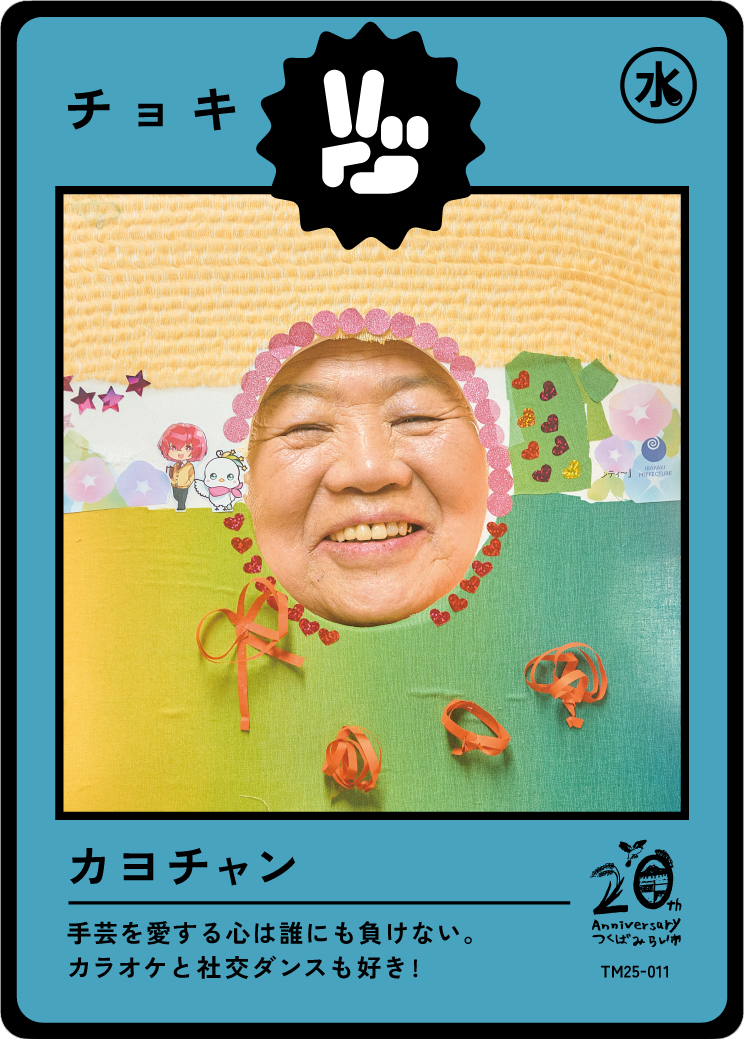 A playful card featuring a person's face surrounded by colorful paper decorations, with Japanese characters and symbols, including a water symbol, and a small logo celebrating a 20th anniversary.