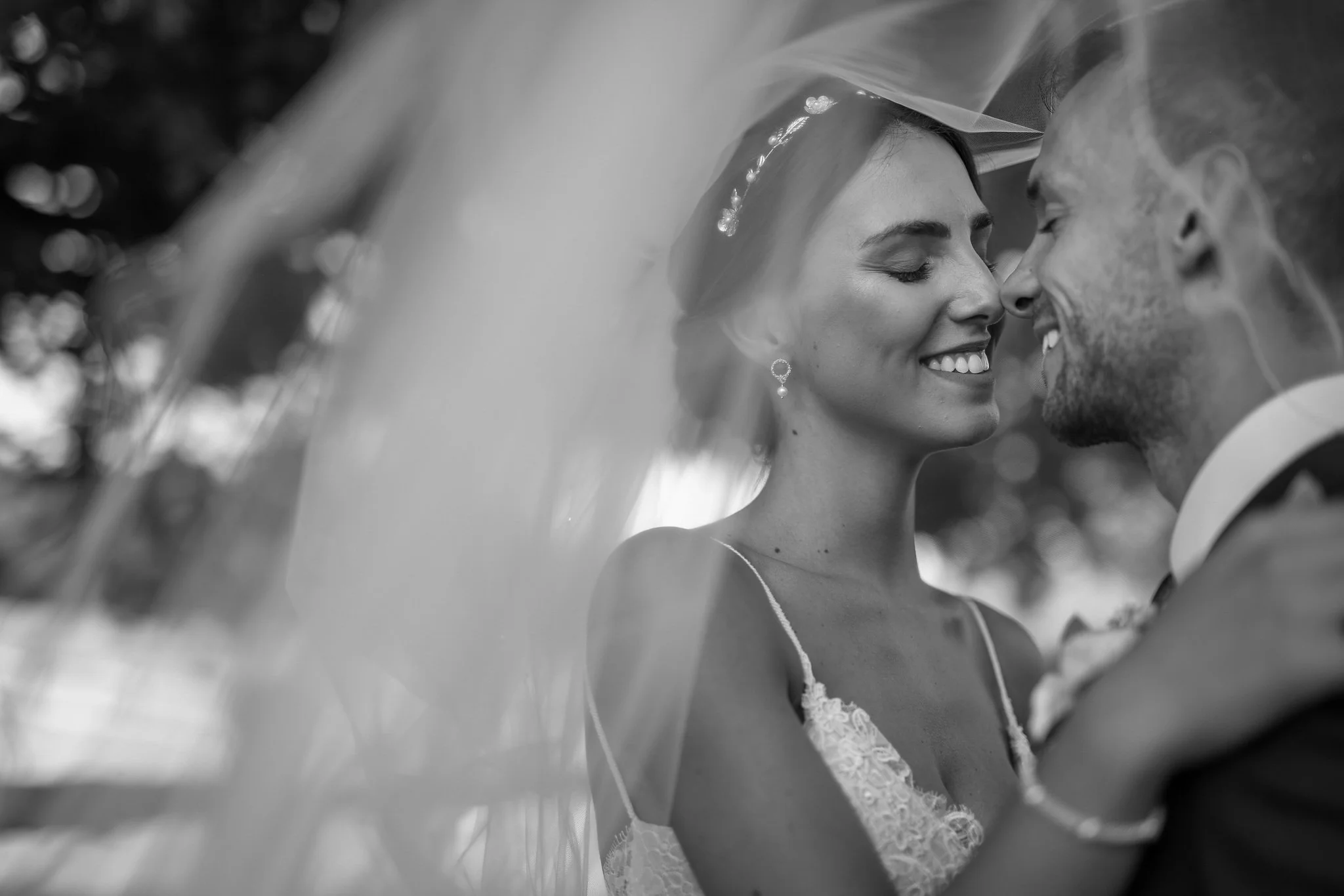 Black and white photograph of a bride and groom with foreheads touching, smiling with eyes closed, closely embracing.