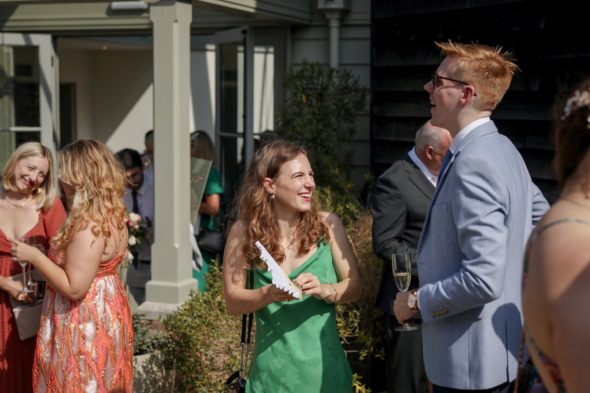 Group of people dressed elegantly, smiling and talking outdoors at a social event, with some holding drinks.