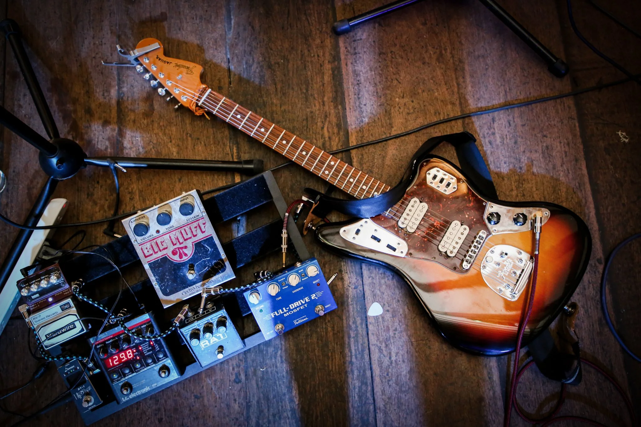 Electric guitar lying on a wooden floor surrounded by audio equipment and cables.