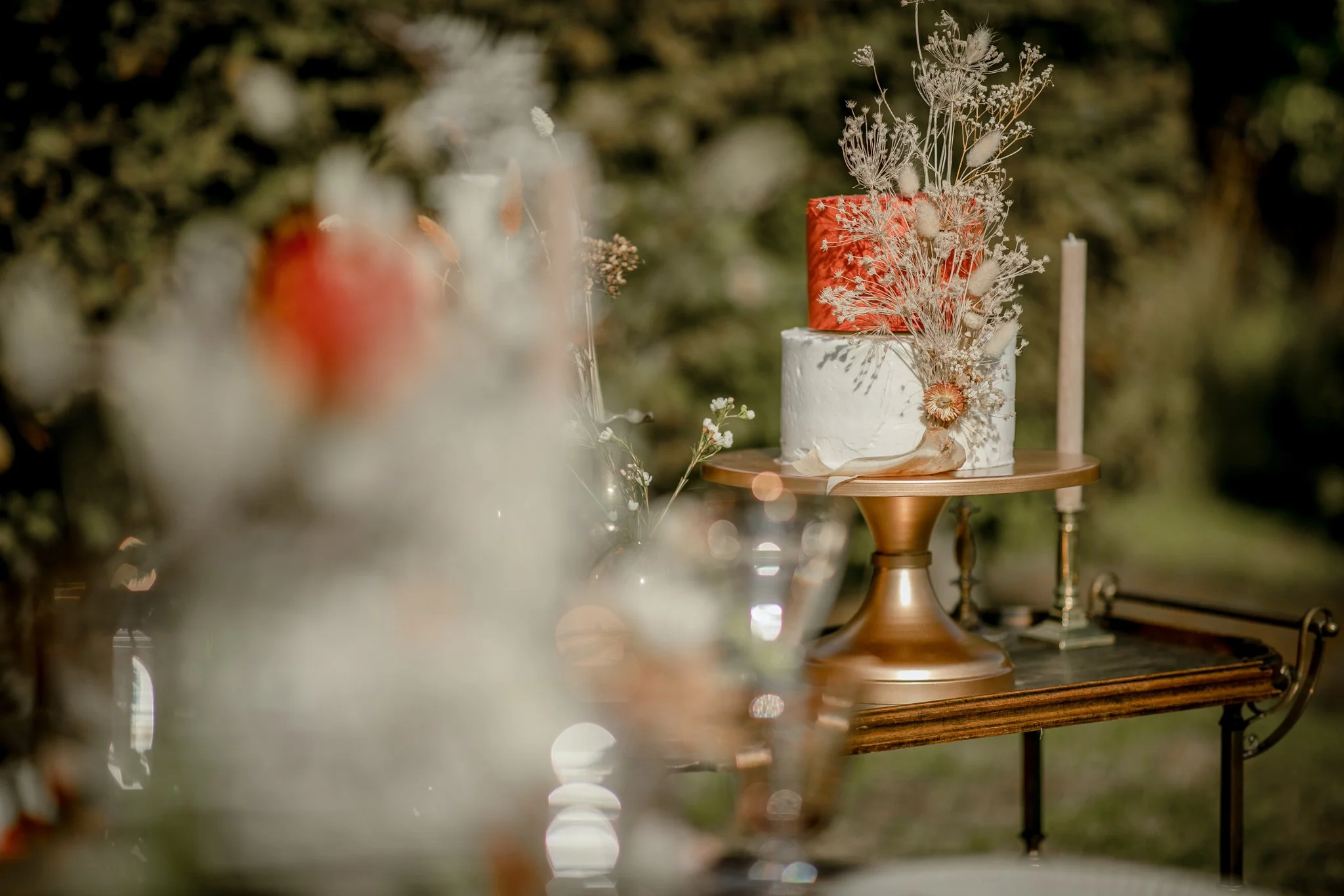 A decorated cake with dried flowers and a candle on a wooden table outdoors.