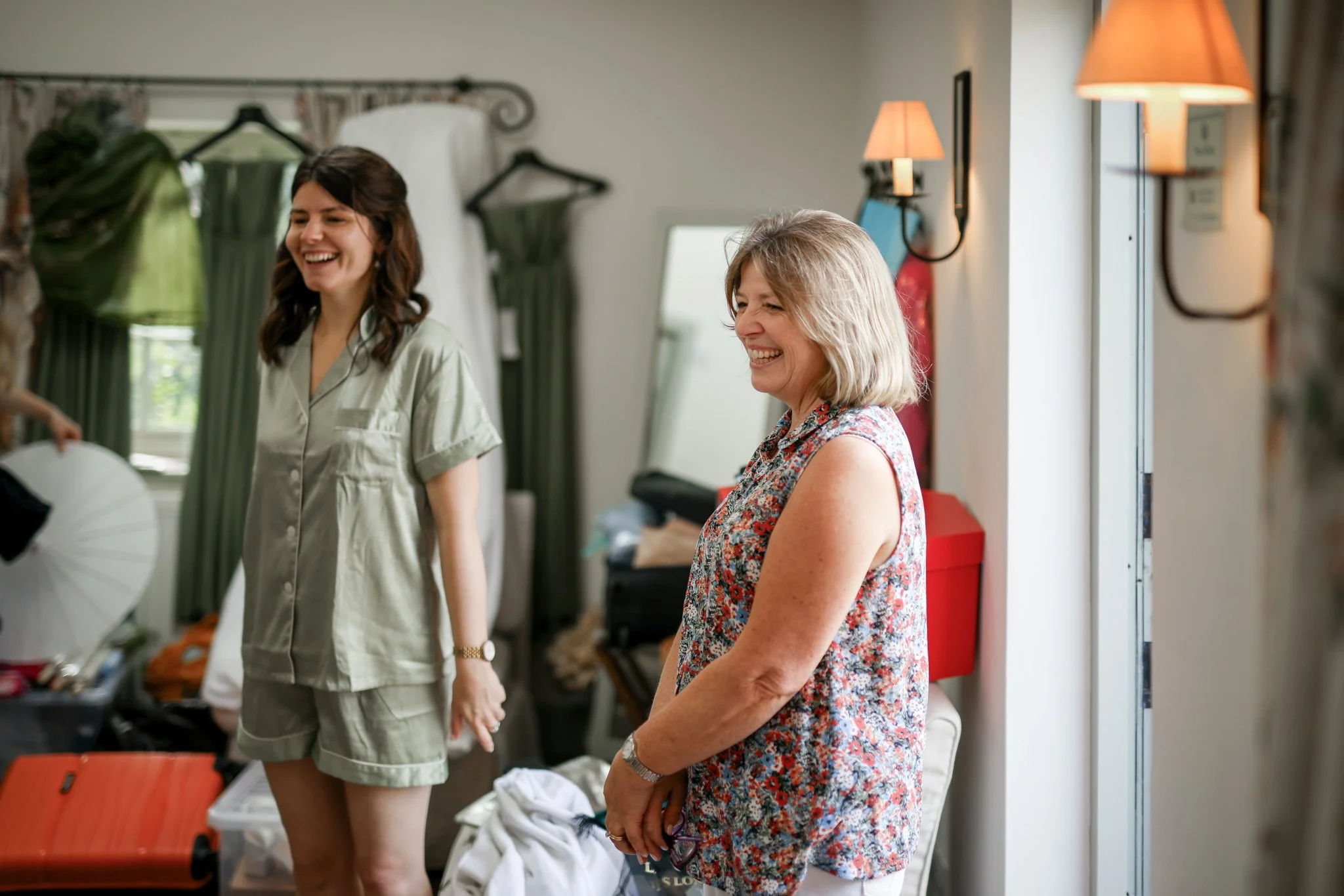 Two women smiling and talking in a room with soft lighting, clothing and equipment around.
