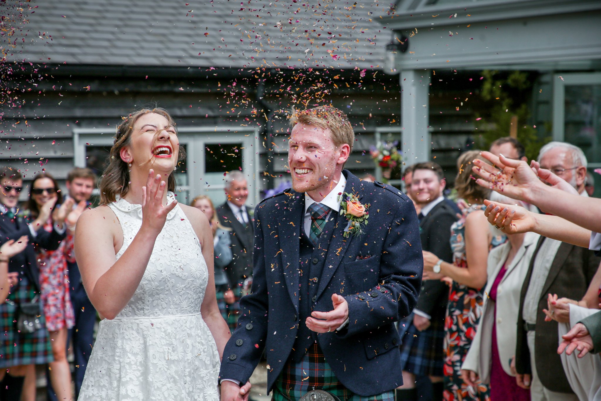A bride and groom celebrating at their outdoor wedding reception, surrounded by guests and colorful confetti.