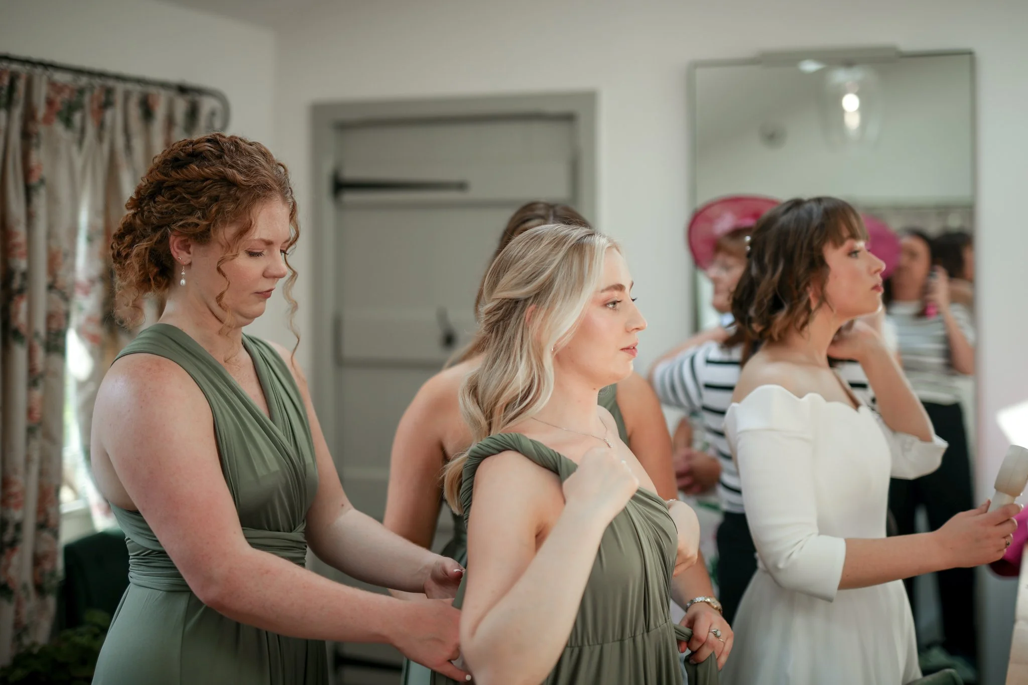 A group of women dressed in formal attire, standing with eyes closed and hands clasped, possibly in prayer or reflection, in a well-lit indoor setting.