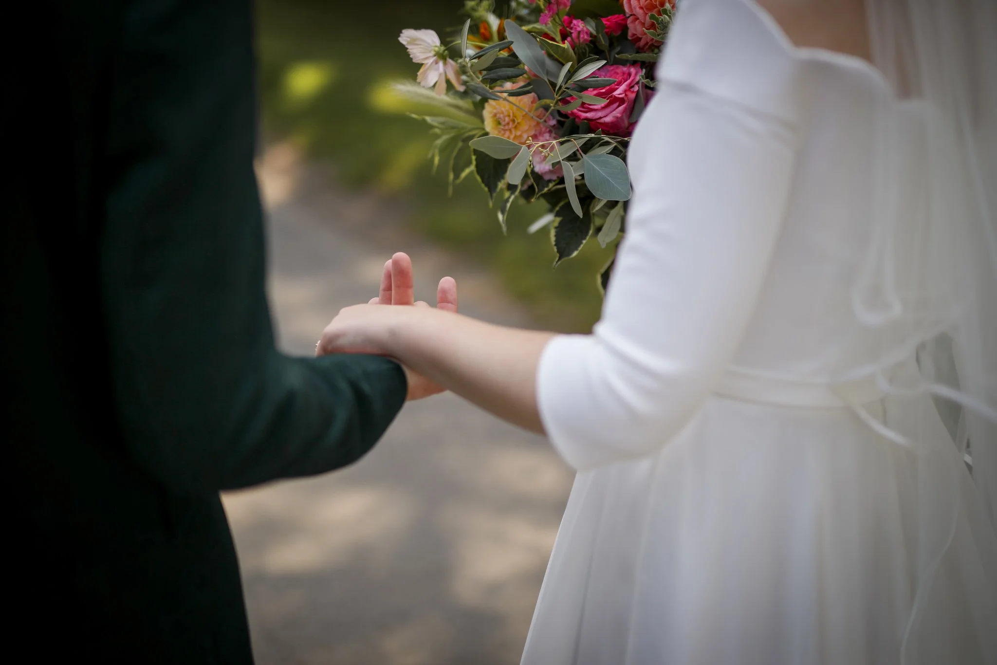 A person in a white dress holding a colorful bouquet of flowers, with another person in a dark suit standing nearby.