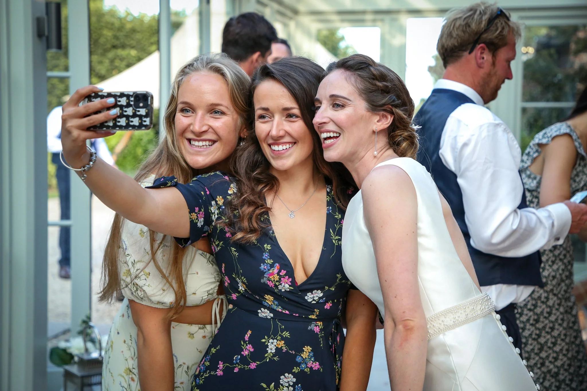 Three women taking a selfie together at an outdoor gathering, surrounded by other people.