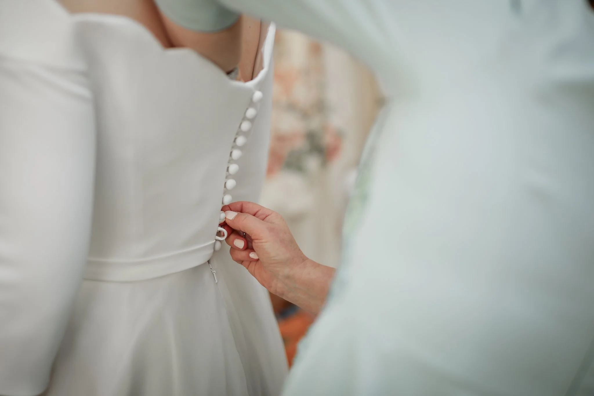 A person fastening the buttons on a white dress with a hand.