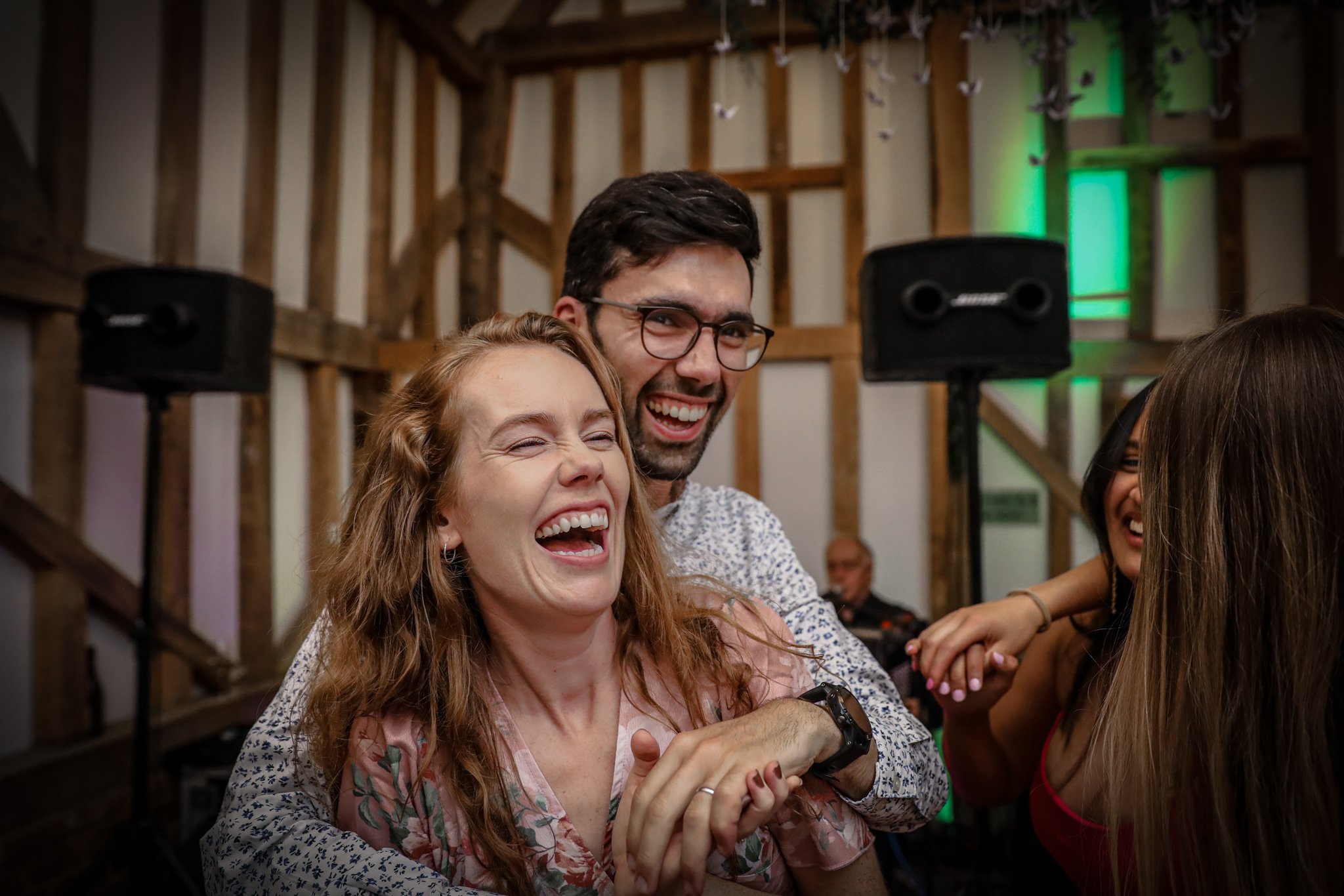People laughing and having fun at a social gathering in a rustic venue with wooden beams and green lighting.