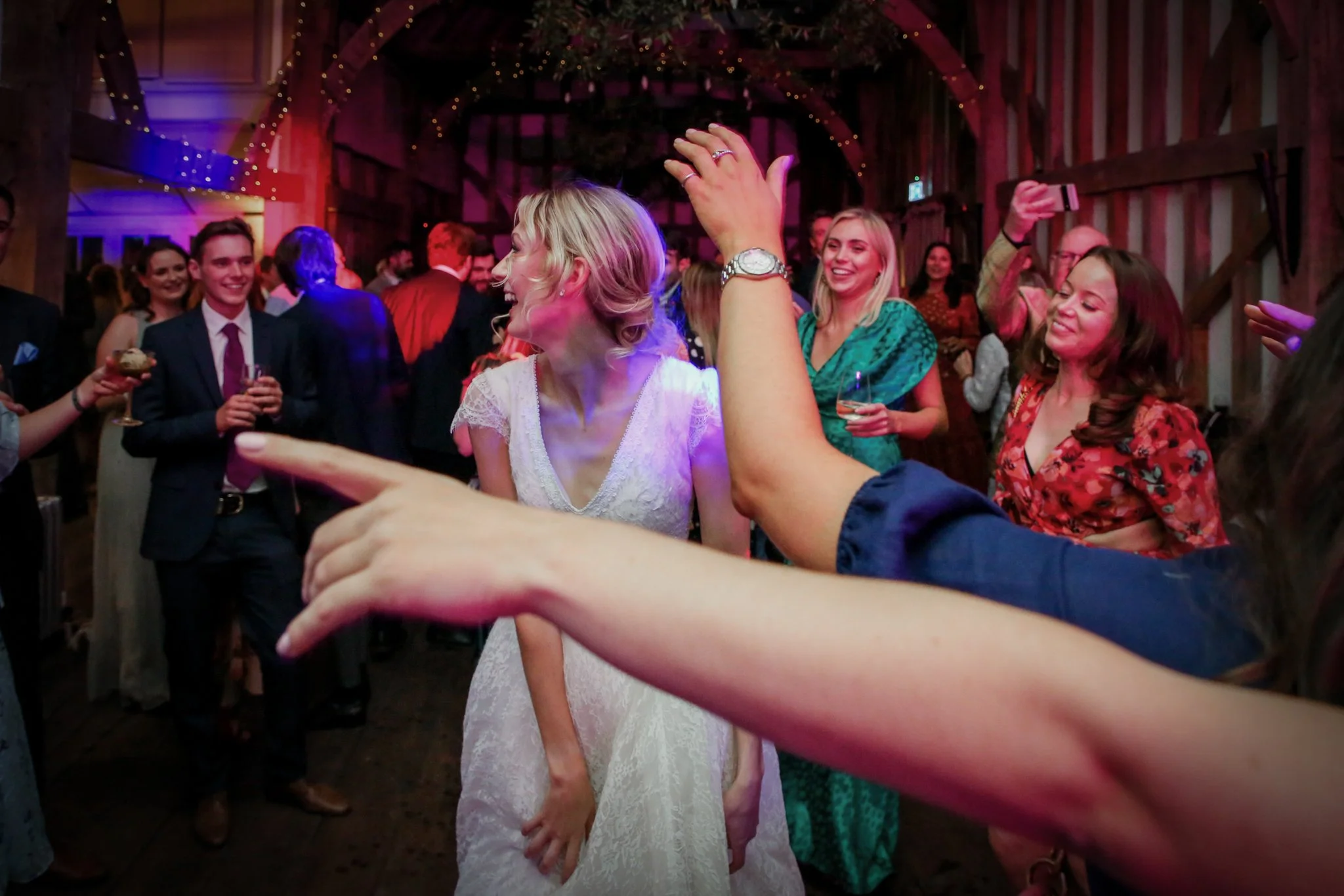 People dancing and celebrating at a wedding reception in a rustic barn, with smiles and a lively atmosphere.
