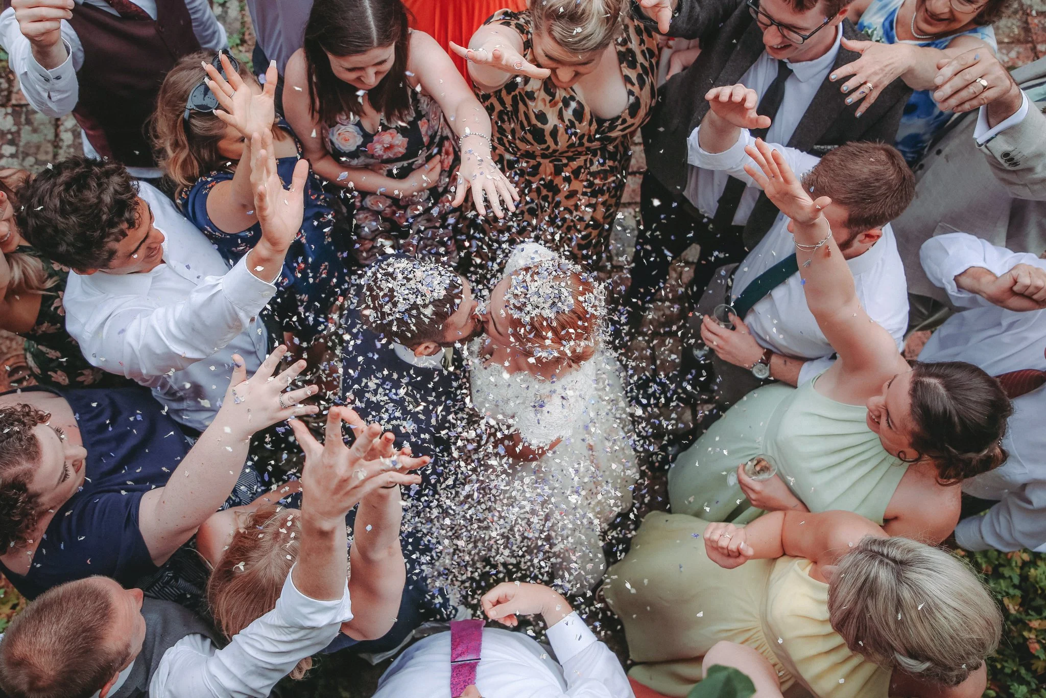 A group of people celebrating a wedding outdoors, throwing confetti and engaging joyfully.