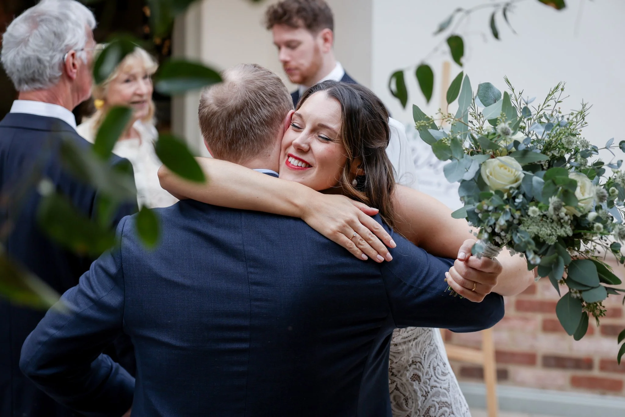A woman hugging a man, holding a bouquet of flowers, at a wedding ceremony.
