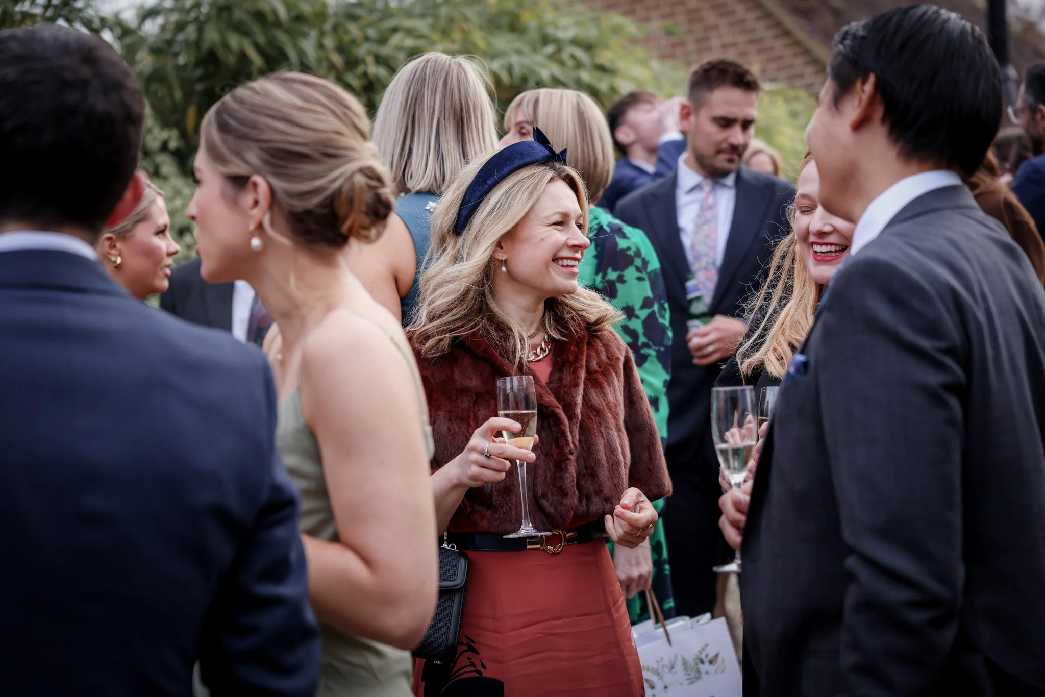 A group of well-dressed people socializing outdoors, holding glasses of champagne, at what appears to be a formal gathering or celebration.