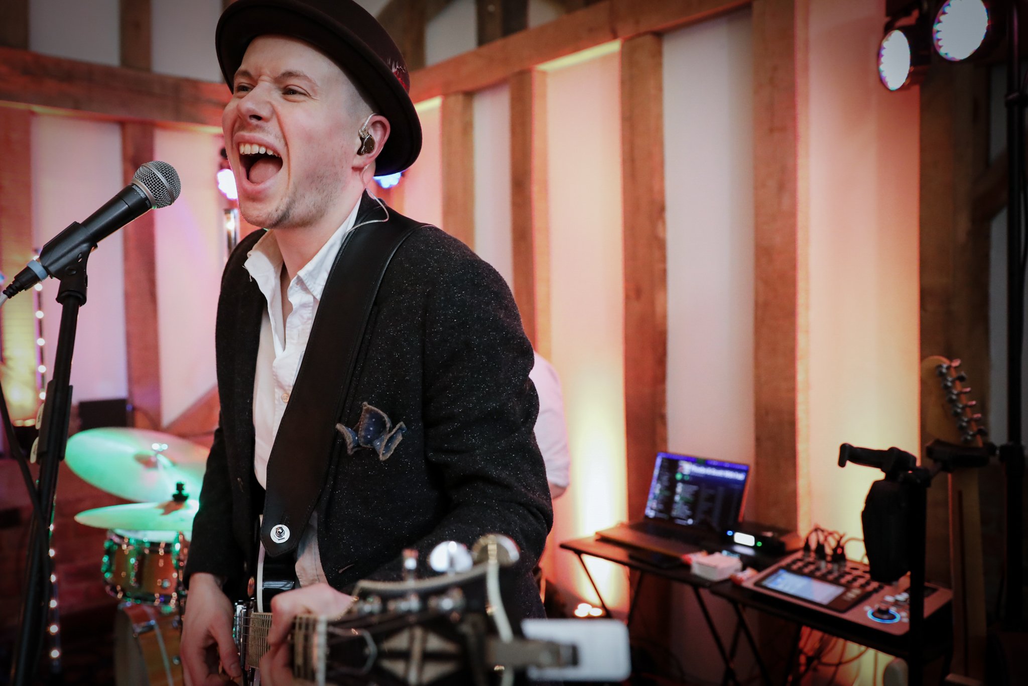 A man singing and playing guitar during a performance in a music studio, with a drum set and music equipment visible in the background.