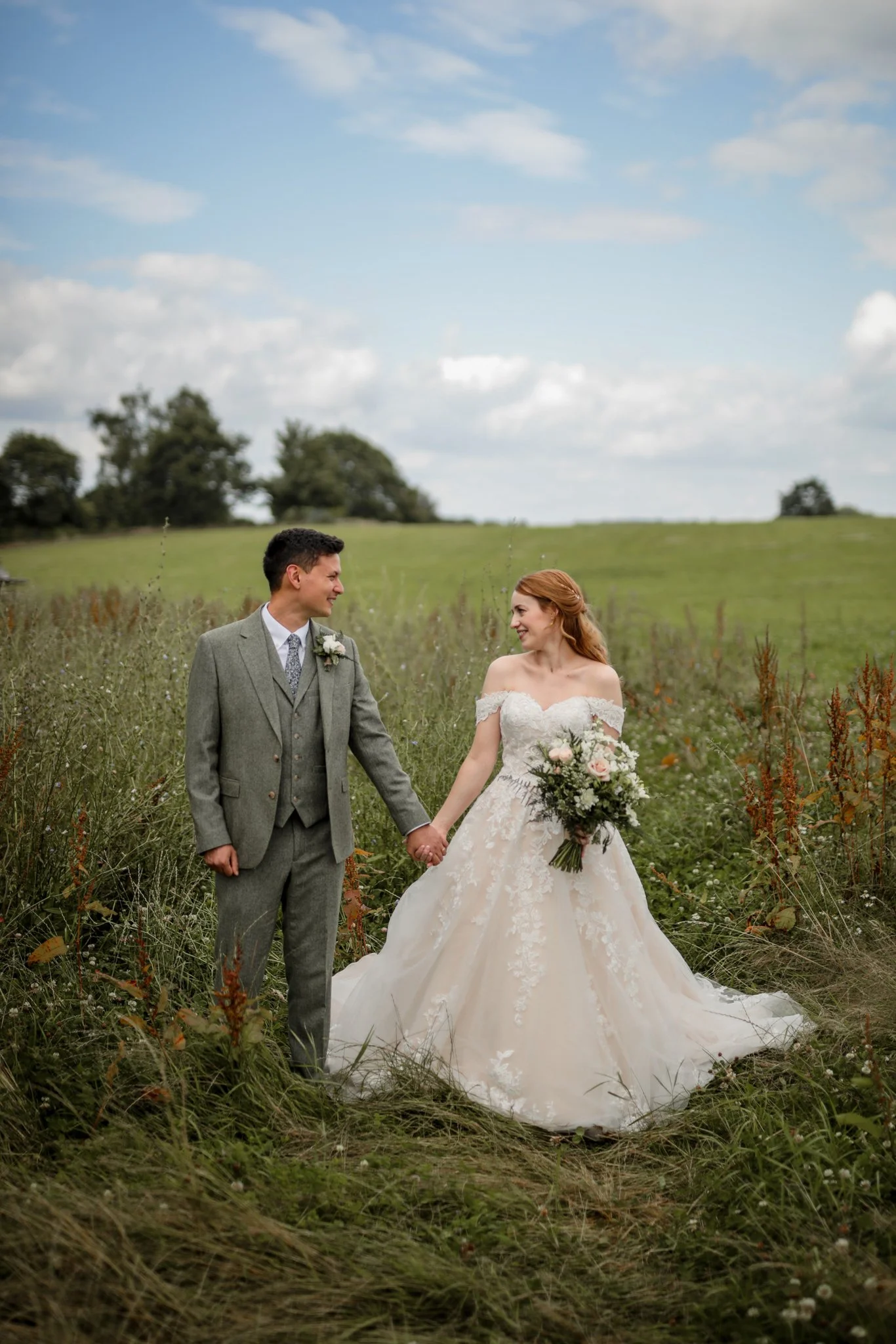 A bride and groom holding hands in a grassy field on a cloudy day.