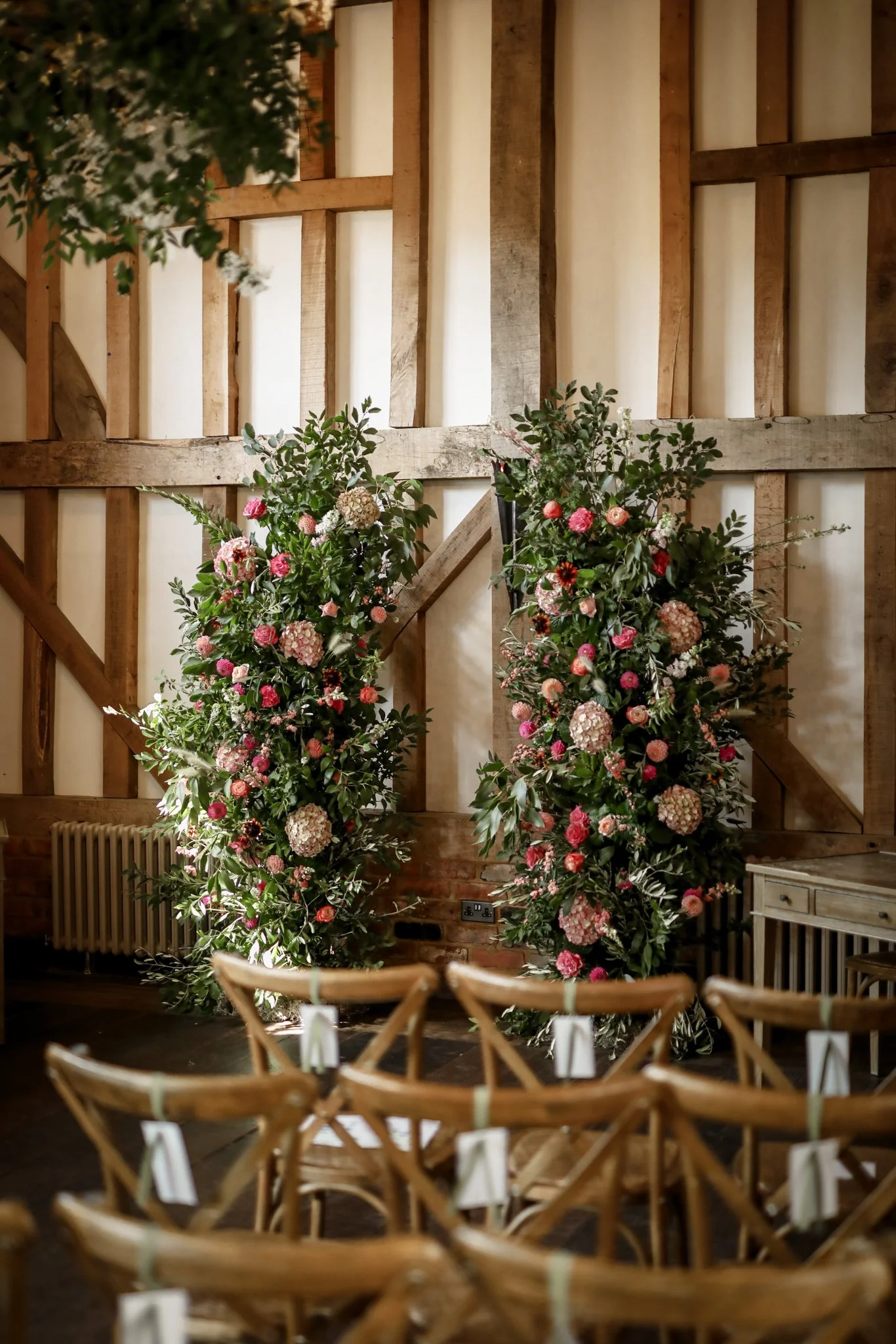 Interior of a rustic event space with large floral arrangements and wooden chairs set up for a gathering.
